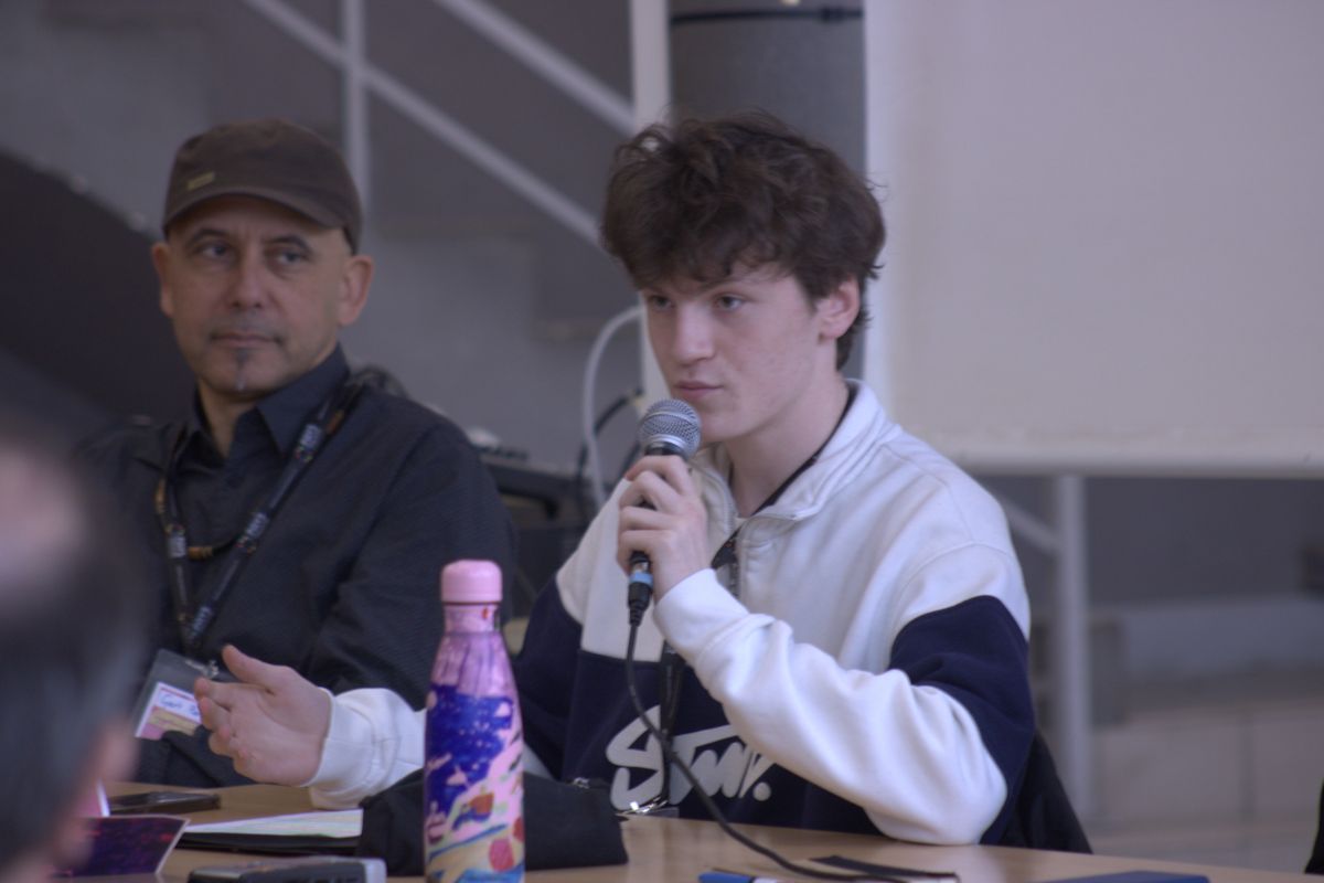 Un lycéen parle dans un micro pendant la table ronde, avec Gert-Peter Bruch assis à côté de lui.